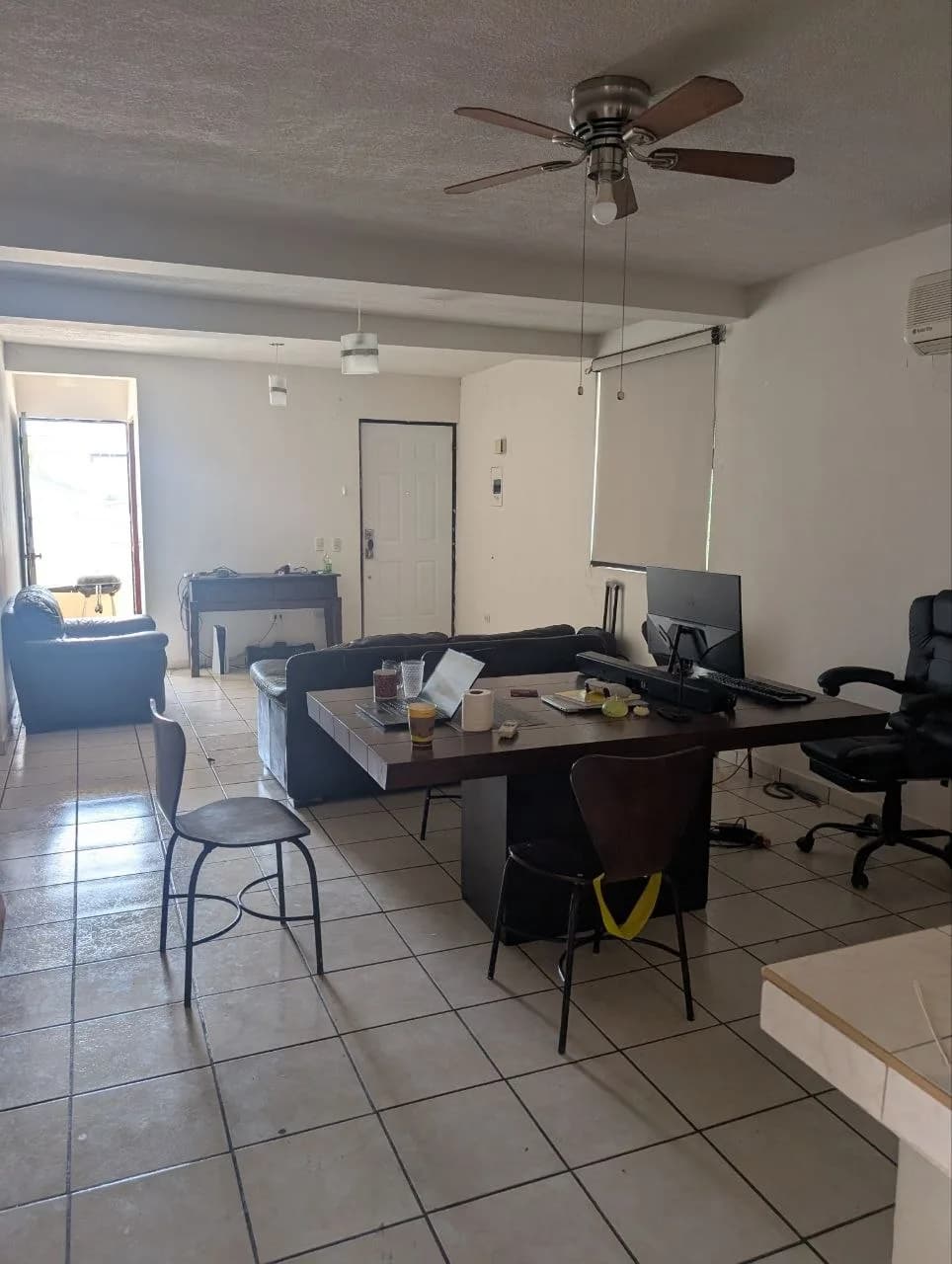 Sala con piso de baldosas, mesa de trabajo con computadora y ventilador de techo